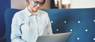 woman sits on a couch as she researches real estate software options on her laptop