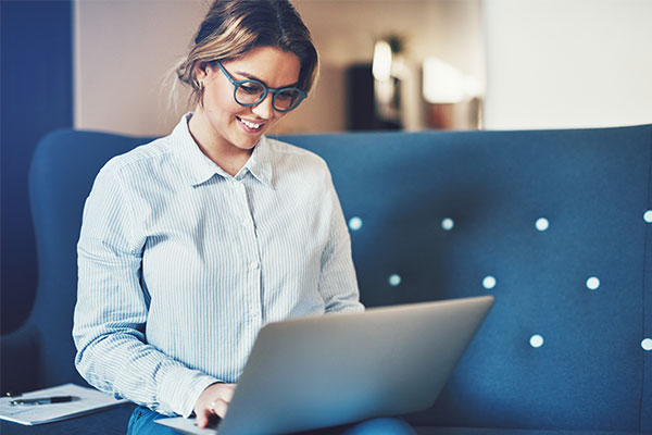 woman sits on a couch as she researches real estate software options on her laptop